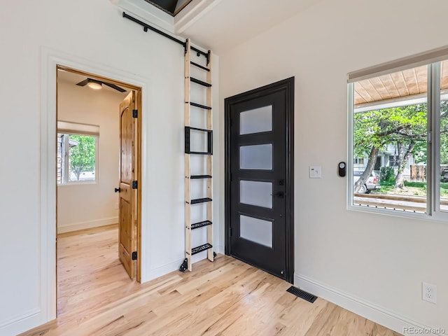 foyer entrance with light wood finished floors, a barn door, and baseboards