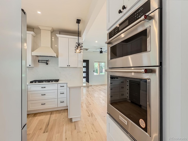 kitchen with custom range hood, stainless steel double oven, a ceiling fan, light wood-type flooring, and recessed lighting