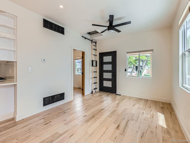 unfurnished living room featuring a barn door, wood finished floors, built in shelves, a ceiling fan, and baseboards