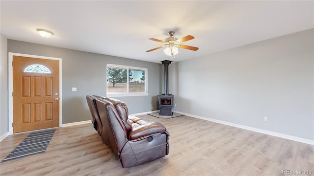 interior space with baseboards, a ceiling fan, a wood stove, and light wood-style floors