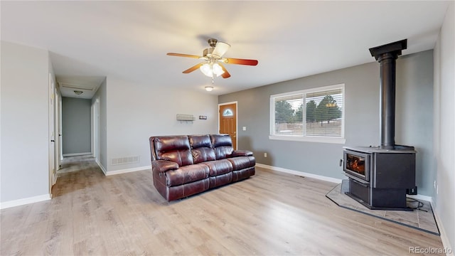 living room featuring a wood stove, light wood-style floors, baseboards, and visible vents