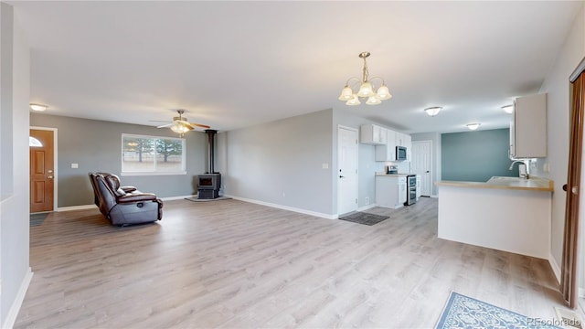 interior space with light wood finished floors, a wood stove, a sink, baseboards, and ceiling fan with notable chandelier