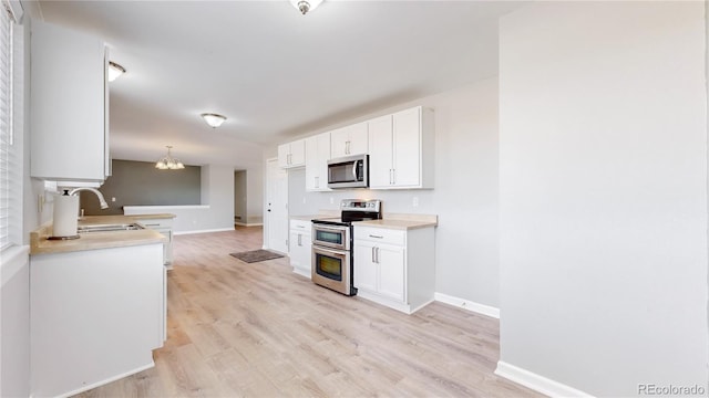 kitchen with stainless steel appliances, a sink, white cabinetry, light wood-type flooring, and an inviting chandelier