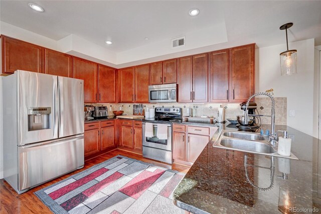 kitchen featuring tasteful backsplash, dark stone counters, light wood-type flooring, pendant lighting, and stainless steel appliances