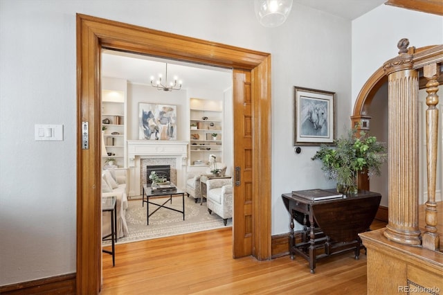 corridor featuring built in shelves, hardwood / wood-style flooring, and an inviting chandelier