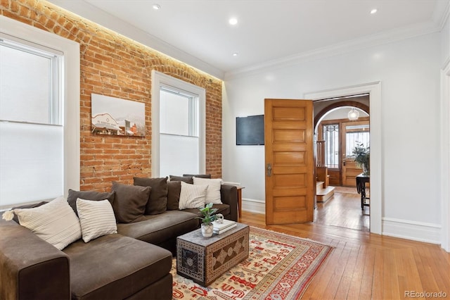 living room with hardwood / wood-style floors, crown molding, and brick wall