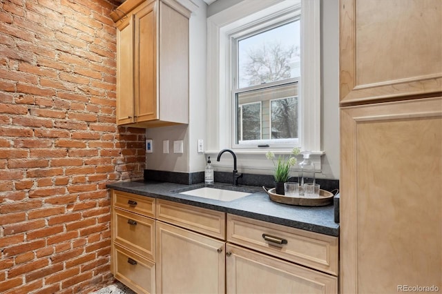 kitchen with brick wall, light brown cabinetry, dark stone countertops, and sink