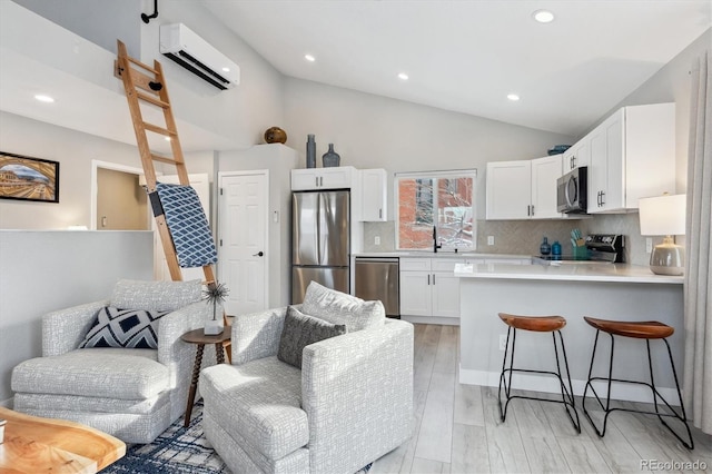 kitchen with a wall mounted air conditioner, light hardwood / wood-style flooring, appliances with stainless steel finishes, tasteful backsplash, and white cabinetry