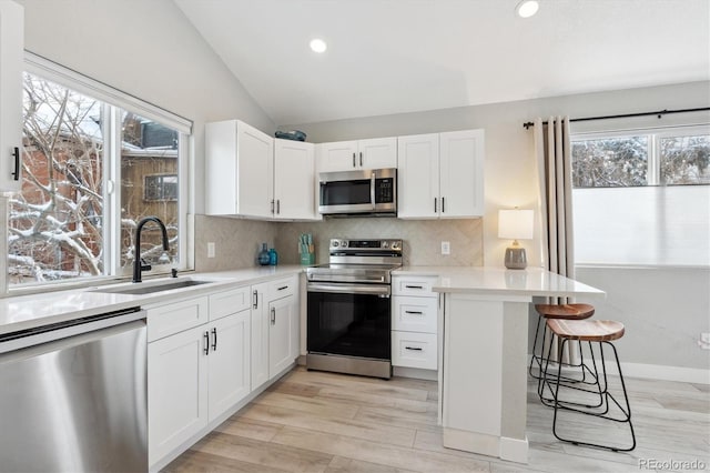 kitchen featuring kitchen peninsula, a kitchen breakfast bar, stainless steel appliances, vaulted ceiling, and sink