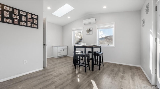 dining room featuring lofted ceiling with skylight, a wall unit AC, baseboards, and wood finished floors