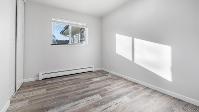 empty room featuring a baseboard heating unit, baseboards, and wood finished floors