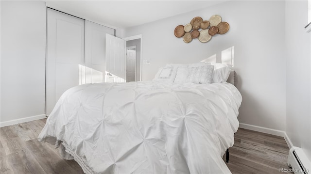 bedroom featuring a baseboard radiator, a closet, baseboards, and wood finished floors