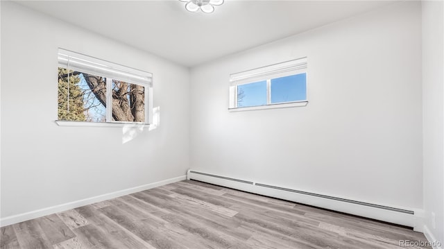 unfurnished room featuring a baseboard heating unit, baseboards, and wood finished floors