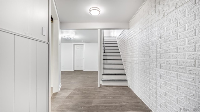 stairs featuring baseboards, brick wall, and wood finished floors