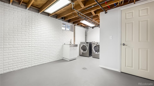 washroom featuring laundry area, brick wall, a sink, and washing machine and clothes dryer