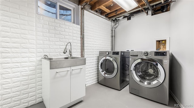 washroom with brick wall, independent washer and dryer, a sink, and cabinet space