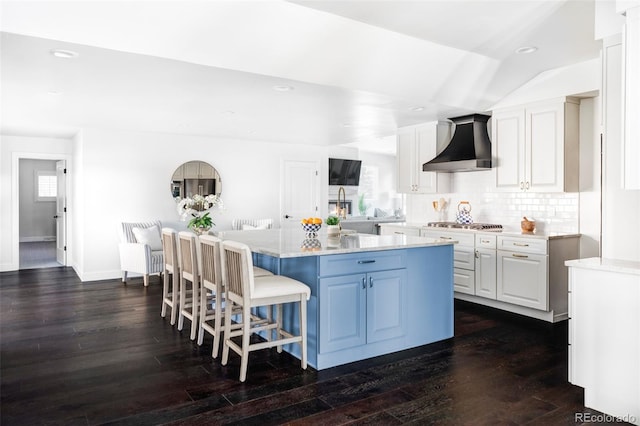 kitchen featuring wall chimney exhaust hood, a breakfast bar area, white cabinetry, a center island, and dark hardwood / wood-style flooring