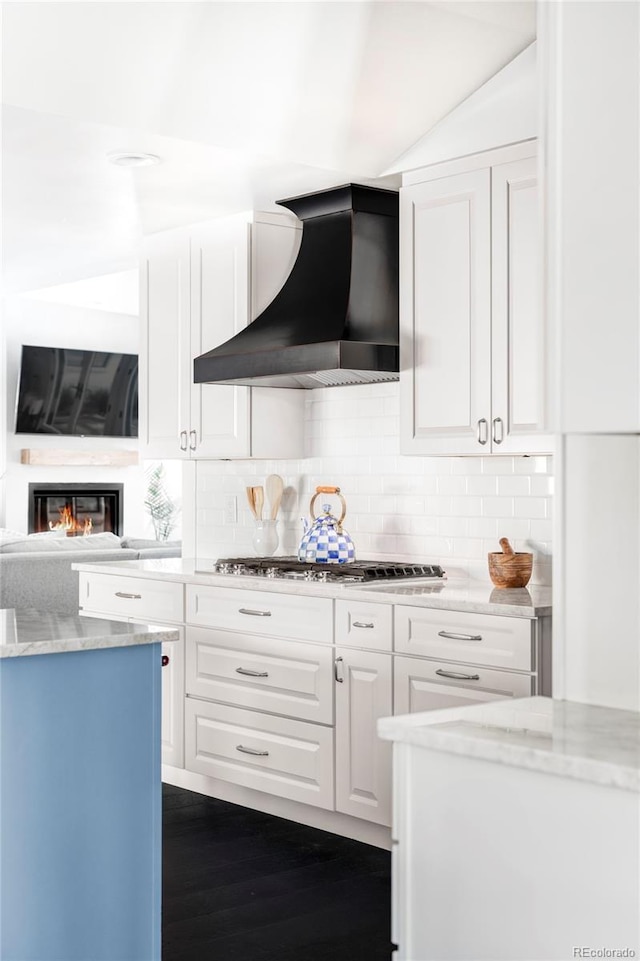 kitchen featuring wall chimney range hood, white cabinetry, tasteful backsplash, light stone countertops, and stainless steel gas stovetop