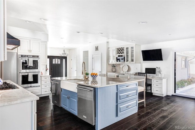 kitchen featuring appliances with stainless steel finishes, light stone counters, blue cabinets, white cabinets, and a center island with sink