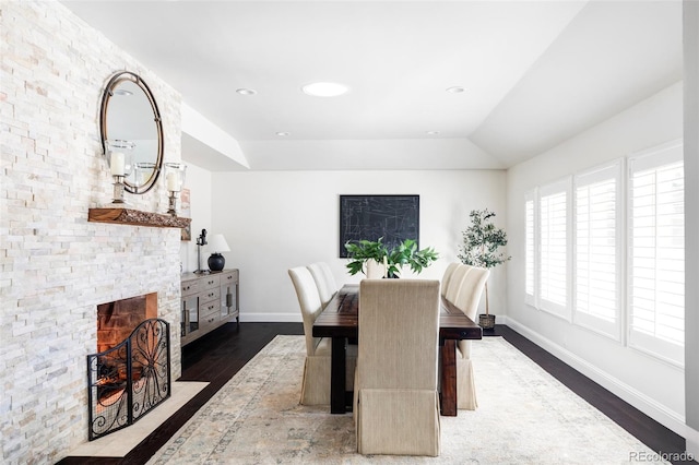 dining space featuring a stone fireplace, vaulted ceiling, and dark hardwood / wood-style floors