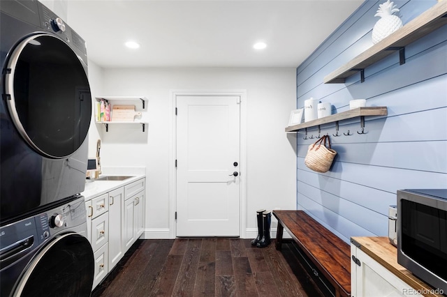 laundry area with wood walls, sink, cabinets, stacked washer / drying machine, and dark wood-type flooring