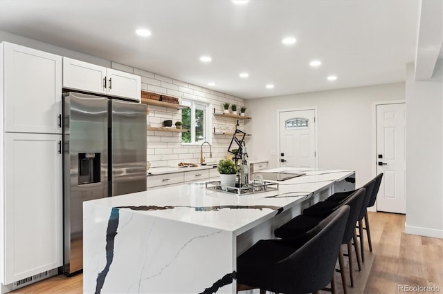 kitchen with white cabinetry, light wood-type flooring, a kitchen island, and stainless steel refrigerator with ice dispenser