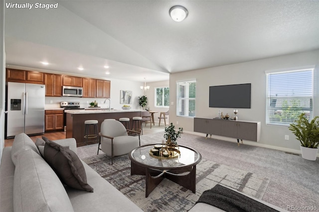 carpeted living room featuring sink, a healthy amount of sunlight, an inviting chandelier, and vaulted ceiling