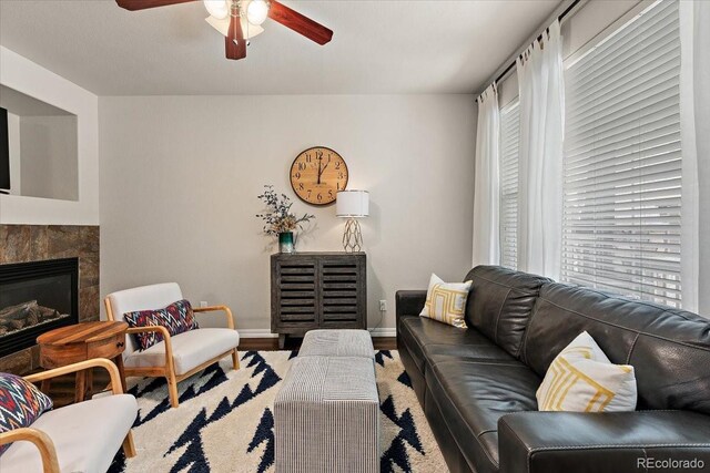 living area featuring a ceiling fan, baseboards, wood finished floors, and a fireplace