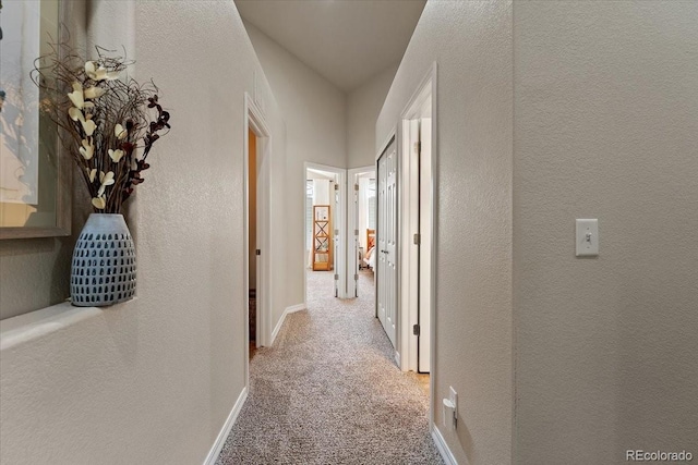 hall featuring carpet floors, a textured wall, and baseboards