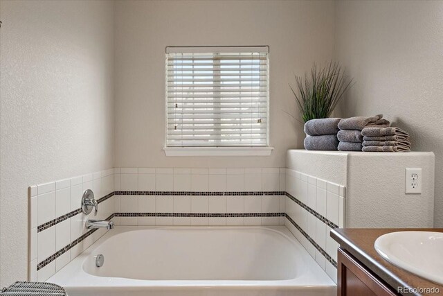 bathroom with vanity, a textured wall, and a bath