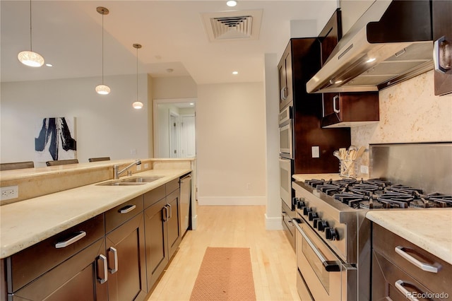kitchen with range hood, a sink, appliances with stainless steel finishes, decorative light fixtures, and light wood finished floors