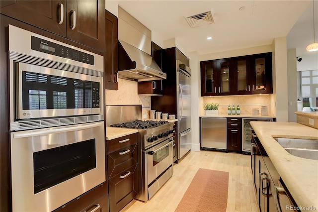 kitchen featuring stainless steel range, fridge, backsplash, light wood finished floors, and glass insert cabinets