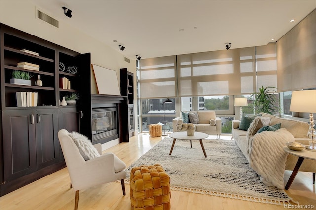 living area with a glass covered fireplace, light wood-style flooring, and a towering ceiling