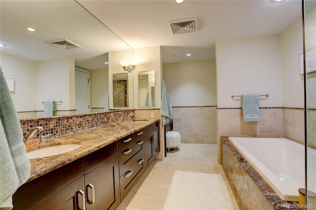 bathroom with a bath, recessed lighting, double vanity, tile patterned floors, and tile walls