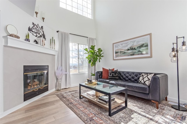 living room featuring light wood-type flooring, a fireplace, and a high ceiling