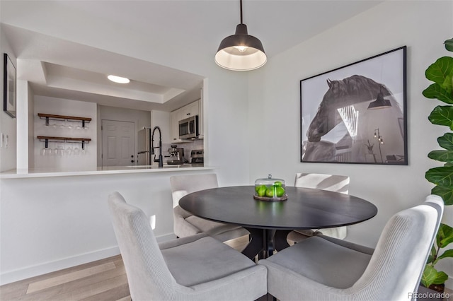 dining space with a tray ceiling, light hardwood / wood-style flooring, and sink