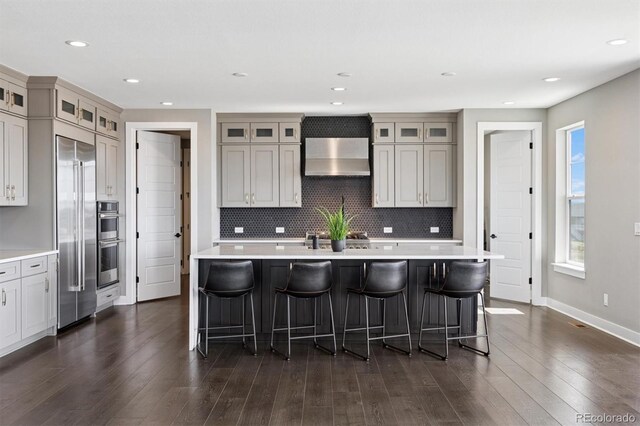 kitchen with appliances with stainless steel finishes, a breakfast bar, light countertops, wall chimney exhaust hood, and decorative backsplash