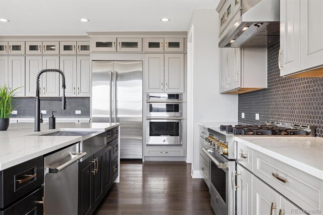 kitchen with a sink, ventilation hood, dark cabinetry, high end appliances, and decorative backsplash