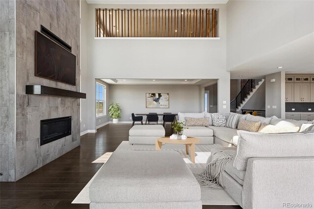 living room featuring stairs, a fireplace, baseboards, a high ceiling, and dark wood-style floors