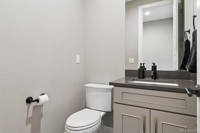 half bathroom featuring toilet, recessed lighting, and vanity