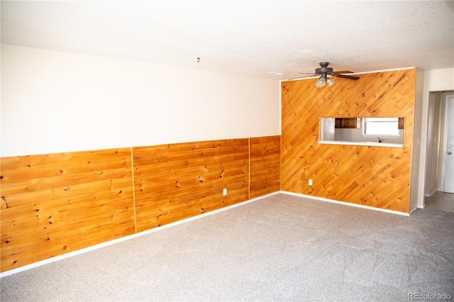 carpeted empty room featuring ceiling fan, wooden walls, and baseboards