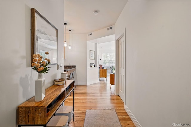 hallway with baseboards, visible vents, and light wood-style floors