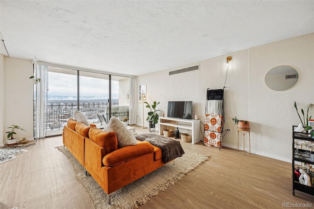 living area with expansive windows, light wood finished floors, a textured ceiling, and visible vents