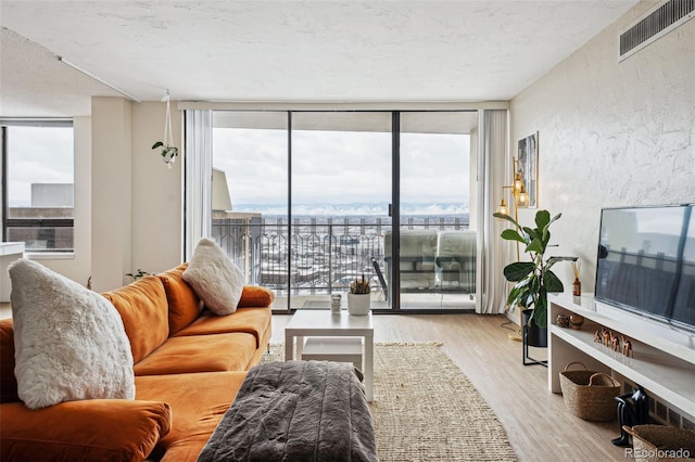 living room with a textured ceiling, a textured wall, light wood-style flooring, visible vents, and expansive windows
