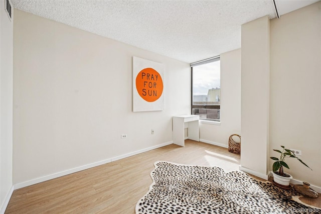 unfurnished room featuring light wood-type flooring, visible vents, a textured ceiling, and baseboards
