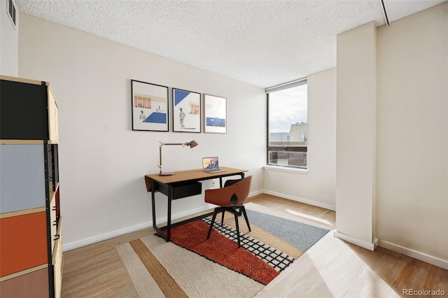 office with light wood-type flooring, baseboards, and a textured ceiling