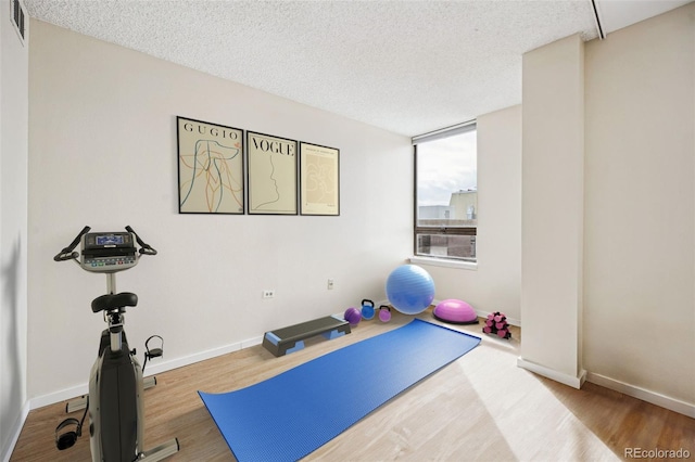workout area with visible vents, a textured ceiling, baseboards, and wood finished floors