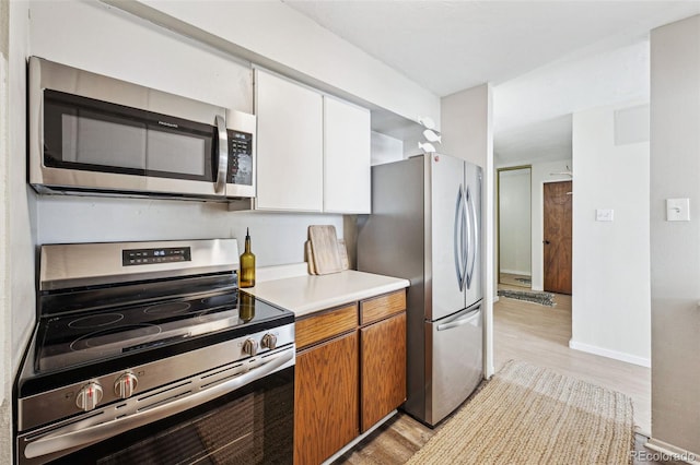 kitchen with white cabinetry, light countertops, appliances with stainless steel finishes, light wood-type flooring, and brown cabinetry