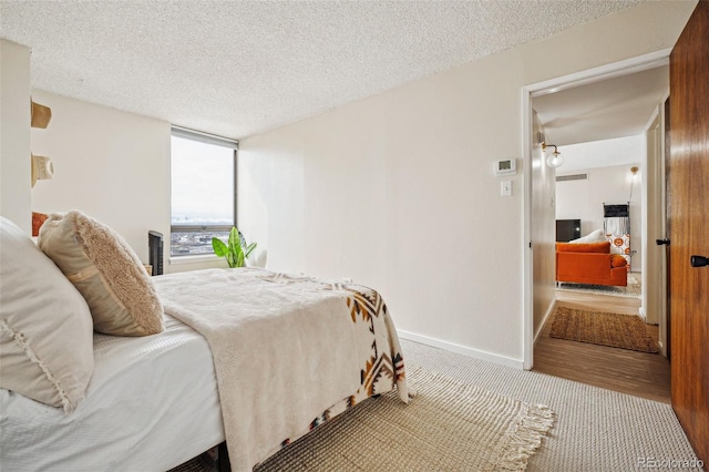 bedroom featuring light carpet, baseboards, and a textured ceiling