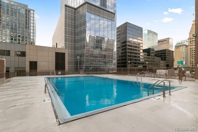 pool with fence, a city view, and a patio